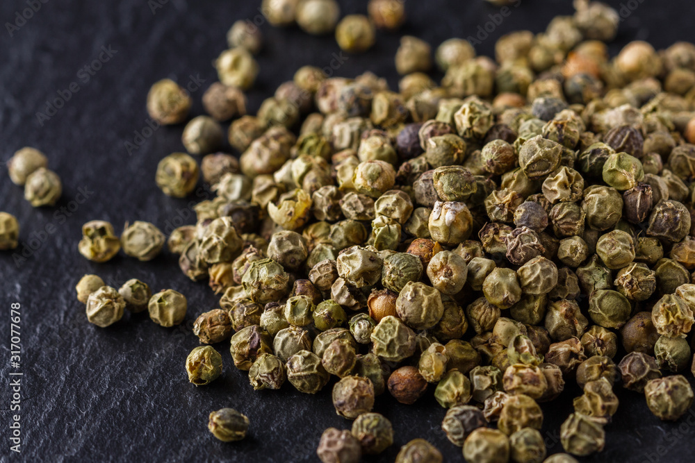 green peppercorns on dark slate stone background