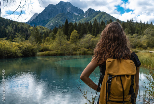 girl with yellow backpack standing in nature in front of a beautiful lake with mountains in the backround. 