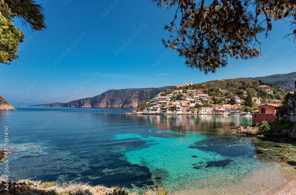 Amazing coastline with colorful houses under sunlight. Wonderful summer seascape with perfect blue sky of Ionian Sea. Assos village. Kefalonia. Greece.