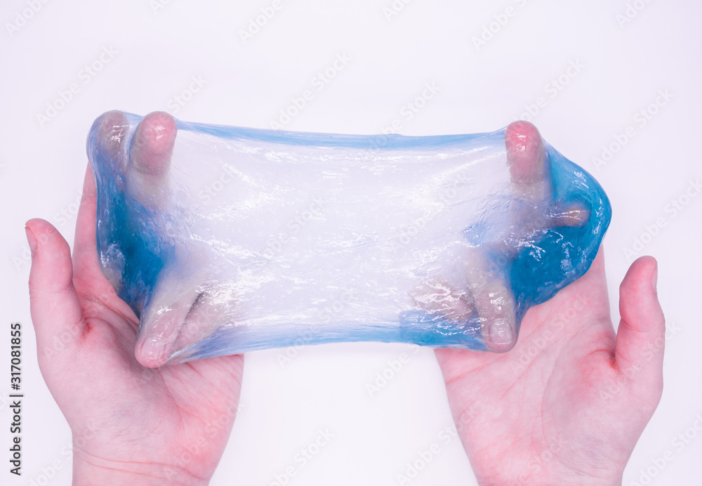 Fototapeta premium Close up of game with light blue slime in someone's hands on a white background. The mucus is crushed, stretched, torn and squeezed by hands