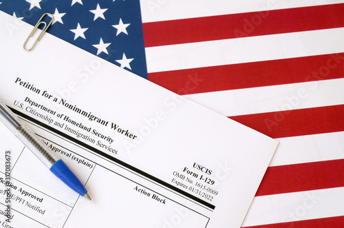 I-129 Petition for a nonimmigrant worker blank form lies on United States flag with blue pen from Department of Homeland Security photo