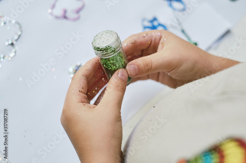 The kid's hands holding the container of green sparkles for making artwork