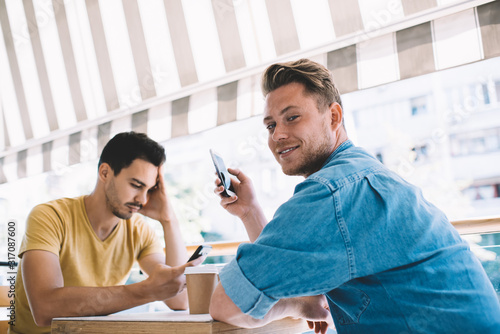 Content guy surfing smartphone taking break with friend in cafe