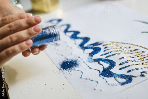 The child dispersing blue glitter sparkles from the jar for create a picture.