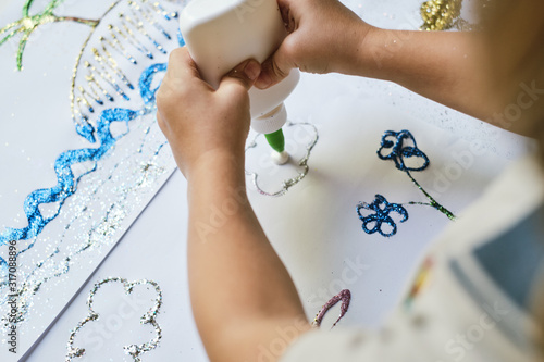 Child's hands applying glue from the jar to the paper for creating art work