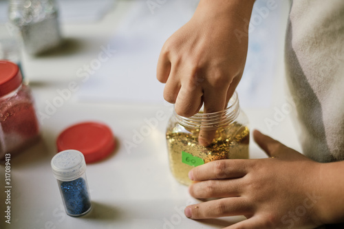 The child puts his fingers in a jar of glitter sparkles