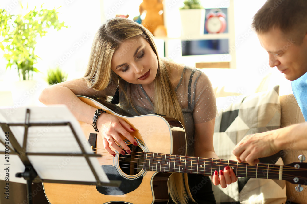 Musical Workshop at Home Couple Playing Guitar. Handsome Young Man Teaching his Girlfriend Performing Bass while Sitting on Sofa Together. Caucasian Woman Taking Music Composing Classes Musical Workshop at Home Couple Playing Guitar. Handsome Young Man Teaching his Girlfriend Performing Bass while Sitting on Sofa Together. Caucasian Woman Taking Music Composing Classes