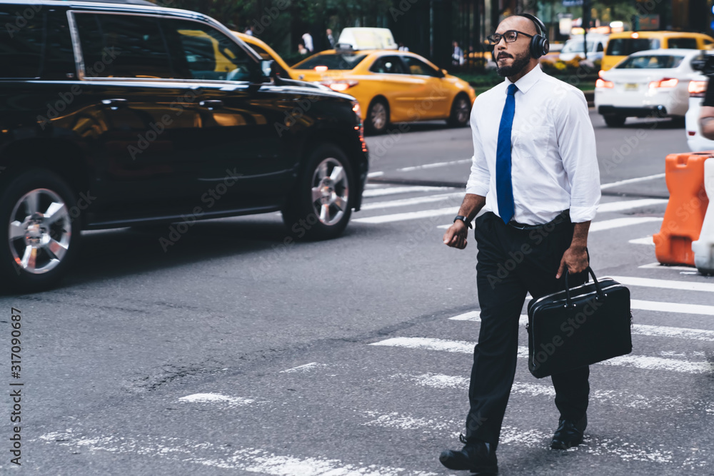 Confident elegant businessman using headphones while walking on street