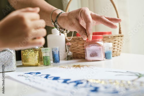 Child's and adult's hands using glitter sparkles for creating a picture