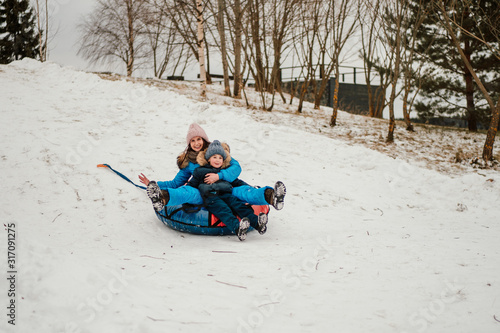 cute boy and his mother riding down the hill on inflatable snow tube in winter