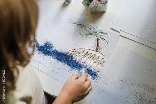 Child using blue glitter sparkles from the jar for create a picture