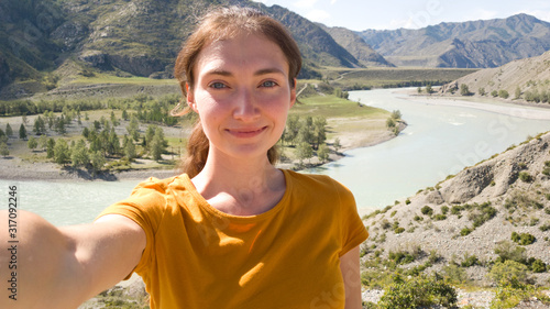 Brunette girl with a ponytail. Takes a selfie on the background of the river. Summer trip in nature. A trip to the Altai