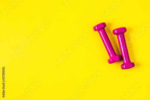 Pink dumbbells on an yellow background, a concept of sports or weight loss