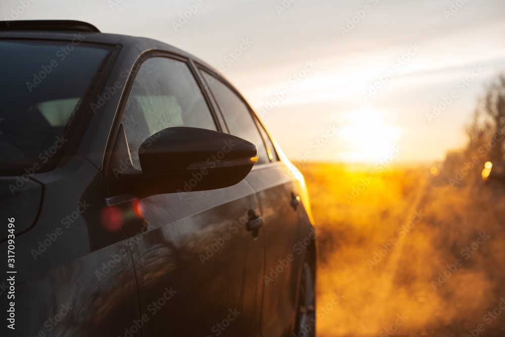 Close-up of car mirror near road on background of sunrise.