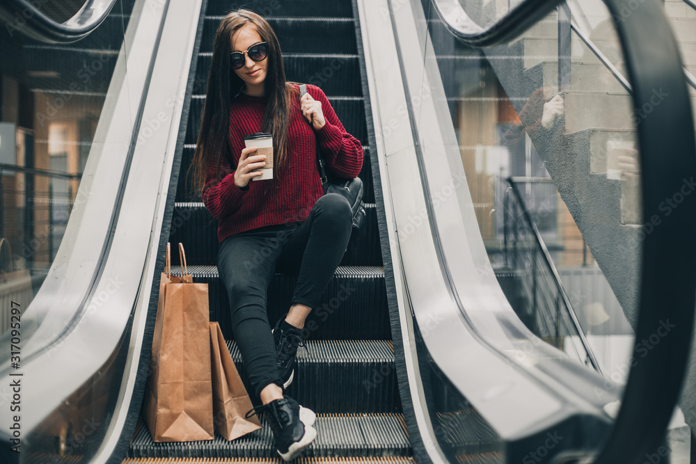 Young pretty woman blogger with smartphone, cup of coffee and shopping bags in city mall