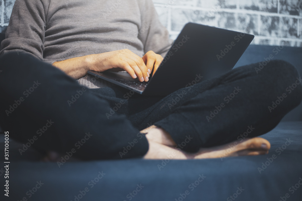Close-up of male hands typing on keyboard of laptop on his legs, man sitting on sofa home. Close-up of male hands typing on keyboard of laptop on his legs, man sitting on sofa home.