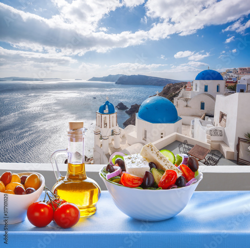 Greek salad against famous church in Oia village, Santorini island in Greece