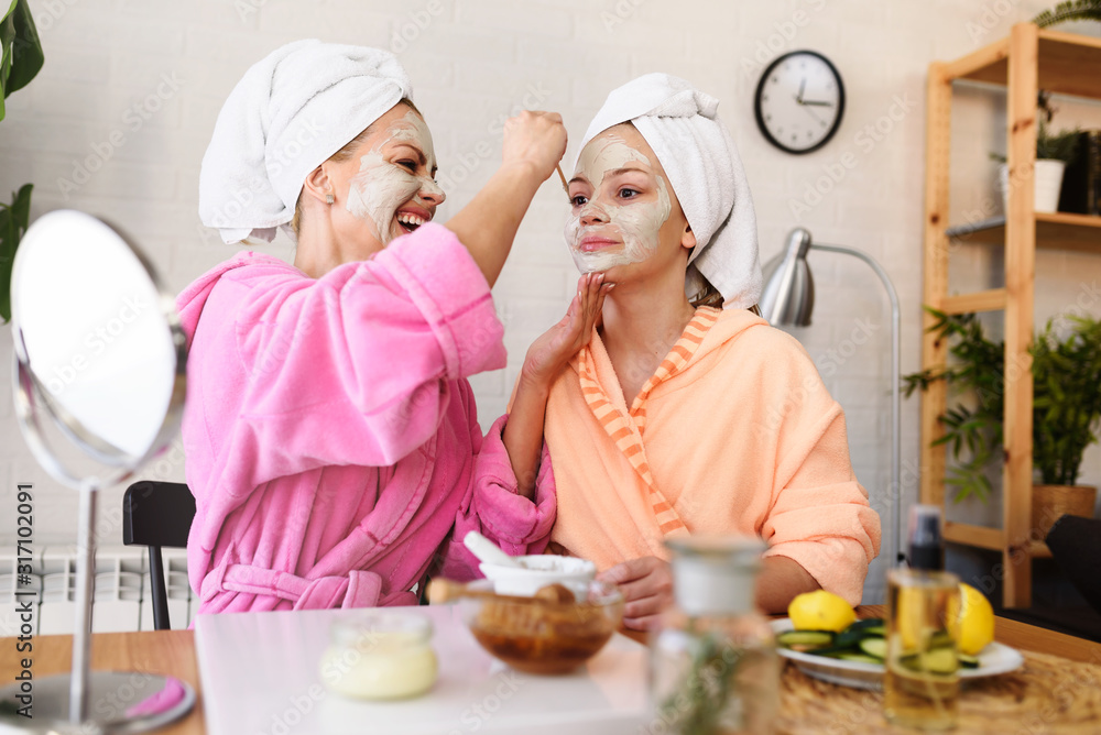 Mother and daughter in bathrobes and towels on head using natural cosmetics and having fun together at home Mother and daughter in bathrobes and towels on head using natural cosmetics and having fun together at home