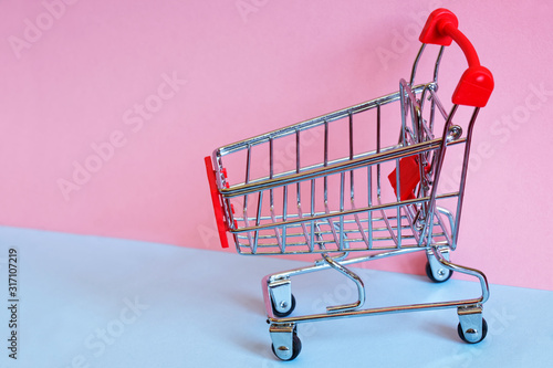 Supermarket metal trolley on light blue and pink background. Close-up