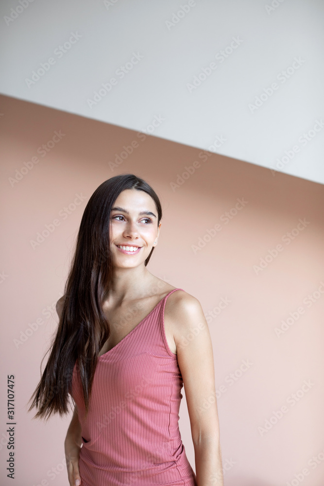 Pretty woman with long hair dressed gray-pink dress smiling while posing against wall. Pretty woman with long hair dressed gray-pink dress smiling while posing against wall.