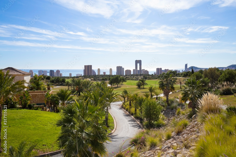 Green golf course and skyscrapers on the horizon and blue sky with beautiful clouds in Benidorm, Spain