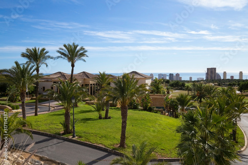 Green golf course and skyscrapers on the horizon and blue sky with beautiful clouds in Benidorm, Spain © Ирина Селина