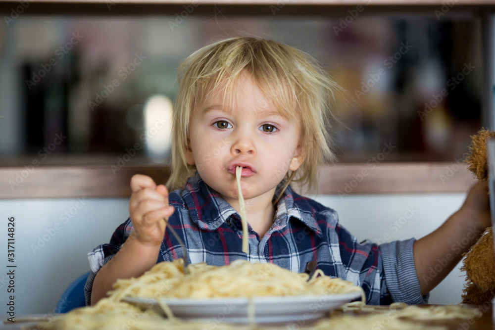 Little baby boy, toddler child, eating spaghetti for lunch and making feeding teddy bear friend Little baby boy, toddler child, eating spaghetti for lunch and making feeding teddy bear friend