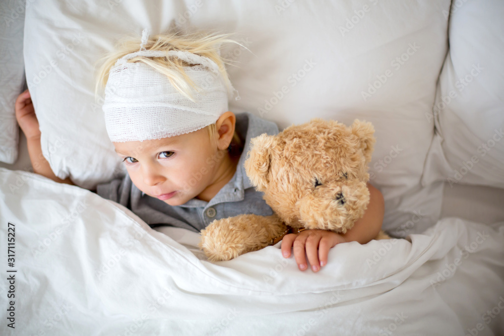 Little toddler boy with head injury, lying in bed, tired