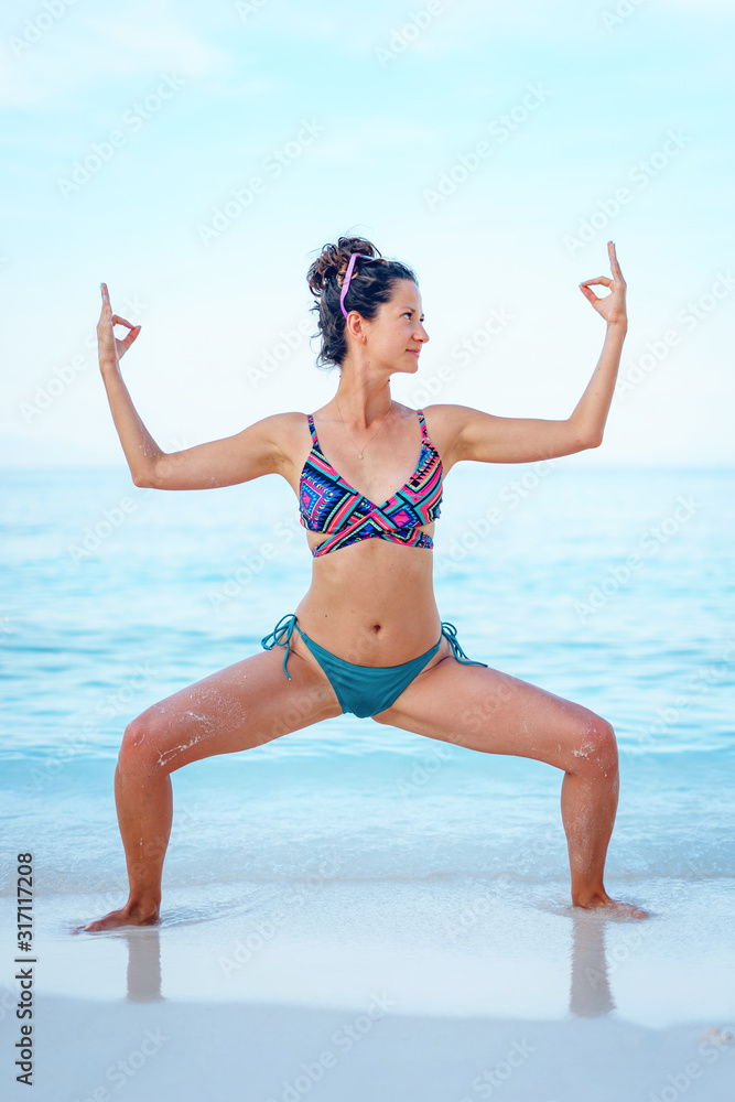 Naklejka premium Young beautiful fit caucasian woman in summer girl bikini swimsuit practice yoga at the beach by the sea or ocean in sunny day stretching on the vacation