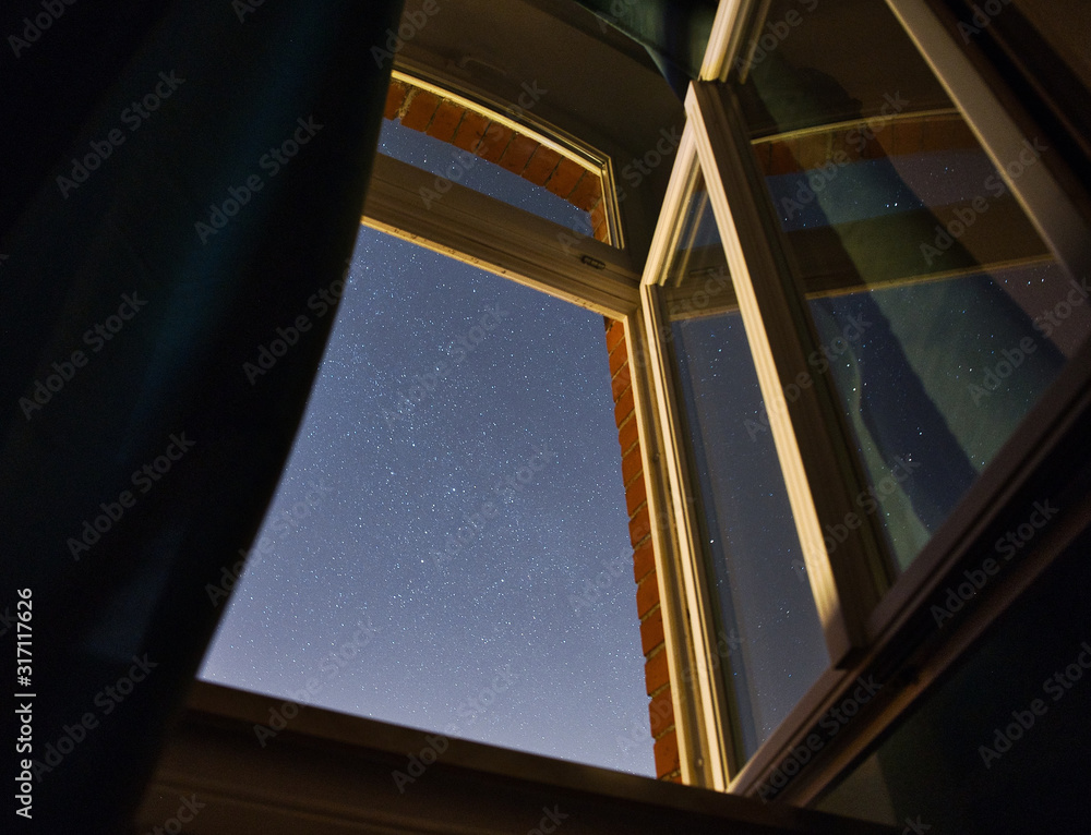 Obraz premium Langzeitbelichtung des Sternenhimmels durch ein geöffnetes Zimmerfenster