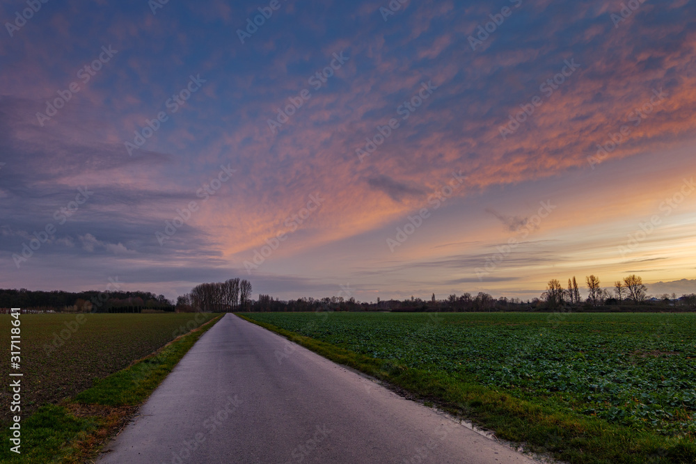 Beautiful dramatic orange and blue cloud and sky after storm and raining over agricultural field and road on countryside area in German. Nimbostratus cloud during sunset. 