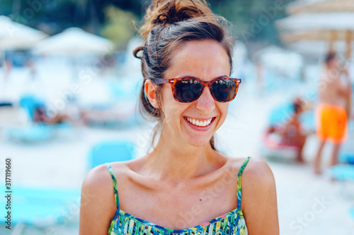 Portrait of young beautiful woman female girl standing on the beach in the sunny summer day wearing sunglasses on the vacation smiling © Miljan Živković
