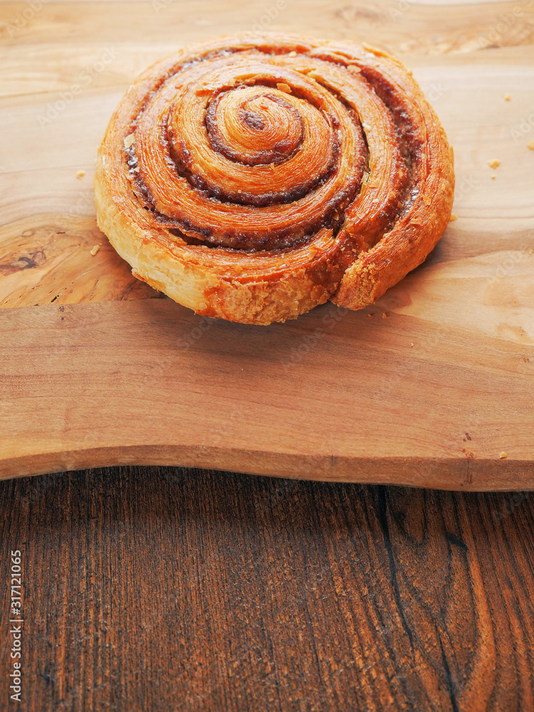 One traditional cinnamon swirl, pastry product on a wooden table surface. Close up. One traditional cinnamon swirl, pastry product on a wooden table surface. Close up.