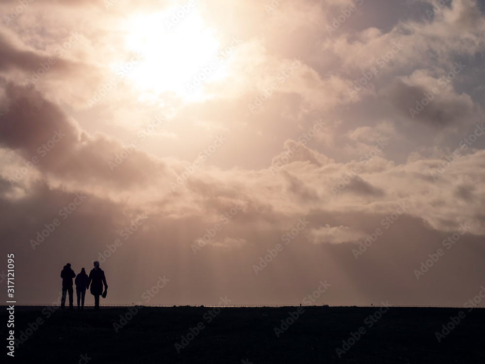 Silhouette of three people on a walk against beautiful warm cloudy sky with sun rays and flare.