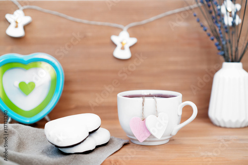 Heart shaped tea bag in white cup of tea with ginger coocies - cute love declaration on wooden background, selective focus. Valentines day concept. Mug of tea for two lovers honeymoon wedding morning
