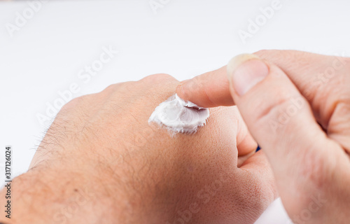 Closeup image of a man applying a hand cream to his hand with his finger. Copy space.