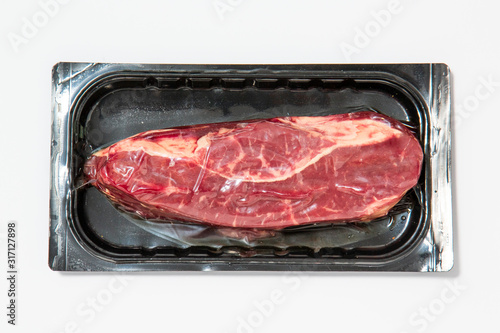 Black plastic pack with fresh beef steak isolated on white background. Raw meat packed without label top view, vacuum packed