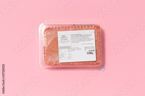 Black plastic pack with fresh hash isolated on pink background. Raw meat packed with label top view, Symbol for environmental pollution done by the food industry