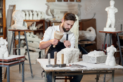 Stone carver works with wooden hammer and chisel at limestone.