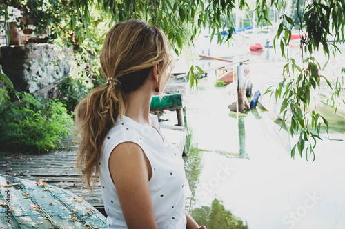Canvas Print side view of woman in white blouse with ponytail looking at boats and sitting in