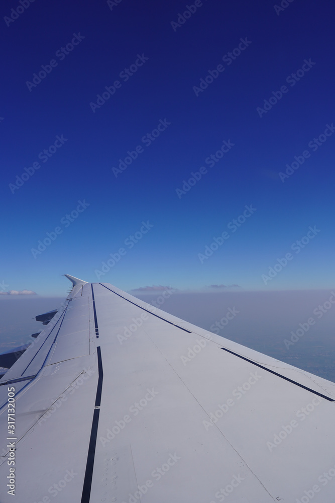 Airplane wing view out of the window on the cloudy sky background. Holiday vacation background. Looking through window of an aircraft during flight, with a nice blue sky