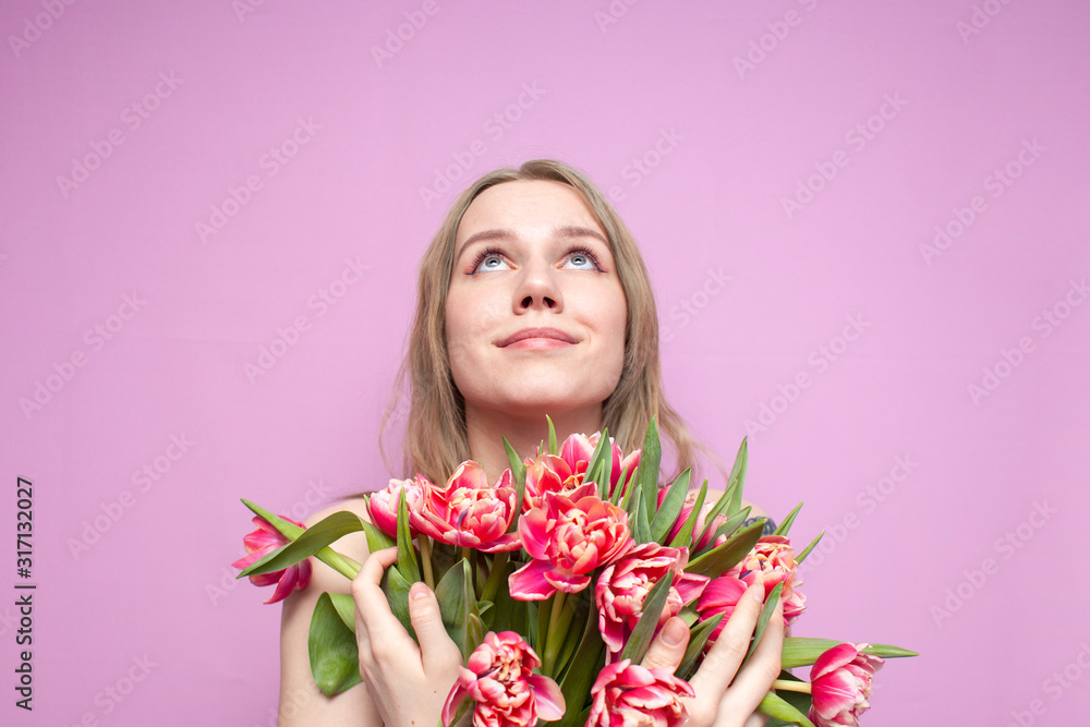 young beautiful girl holds a bouquet of flowers on a pink background, a happy woman with tulips looks up at