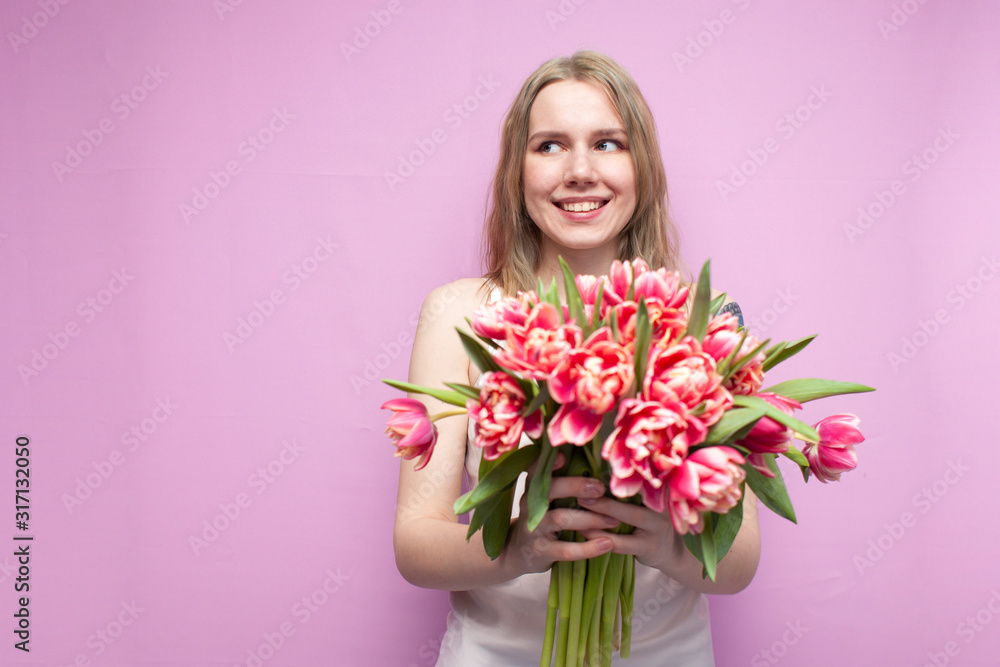 young beautiful girl holds a bouquet of flowers on a pink background, close-up of a bouquet of tulips
