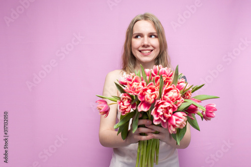 young beautiful girl holds a bouquet of flowers on a pink background  close-up of a bouquet of tulips