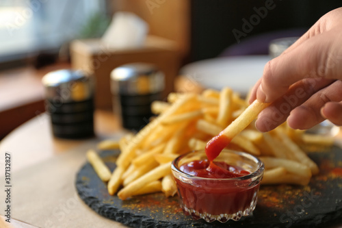 Woman dipping French fries into red sauce in cafe, closeup