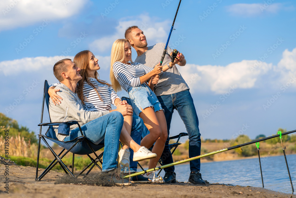 Group of young friends fishing on the pier by lakeside Group of young friends fishing on the pier by lakeside