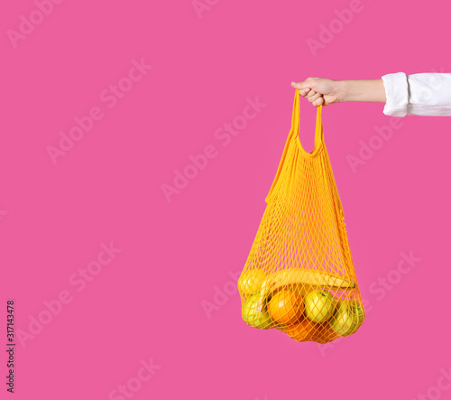 Woman holding net bag with fruits on pink background, closeup