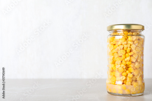 Glass jar of pickled sweet corn on light marble table. Space for text