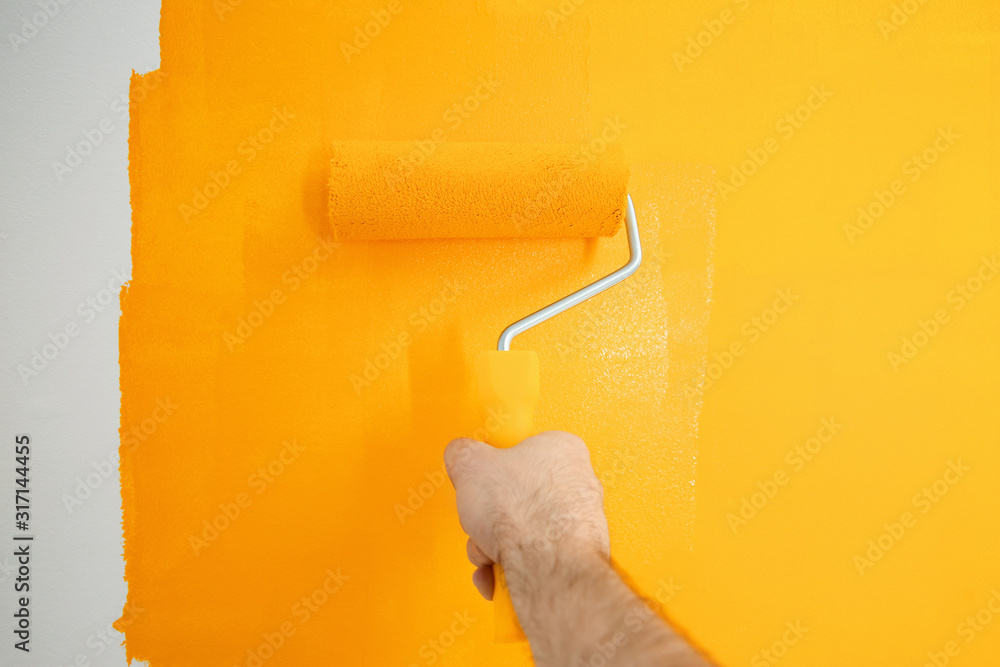 Obraz premium Man painting white wall with yellow dye, closeup. Interior renovation
