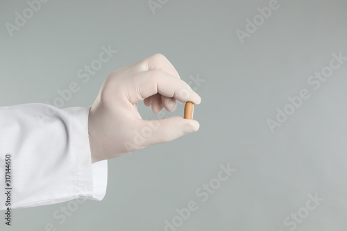 Doctor holding suppository for hemorrhoid treatment on light grey background, closeup